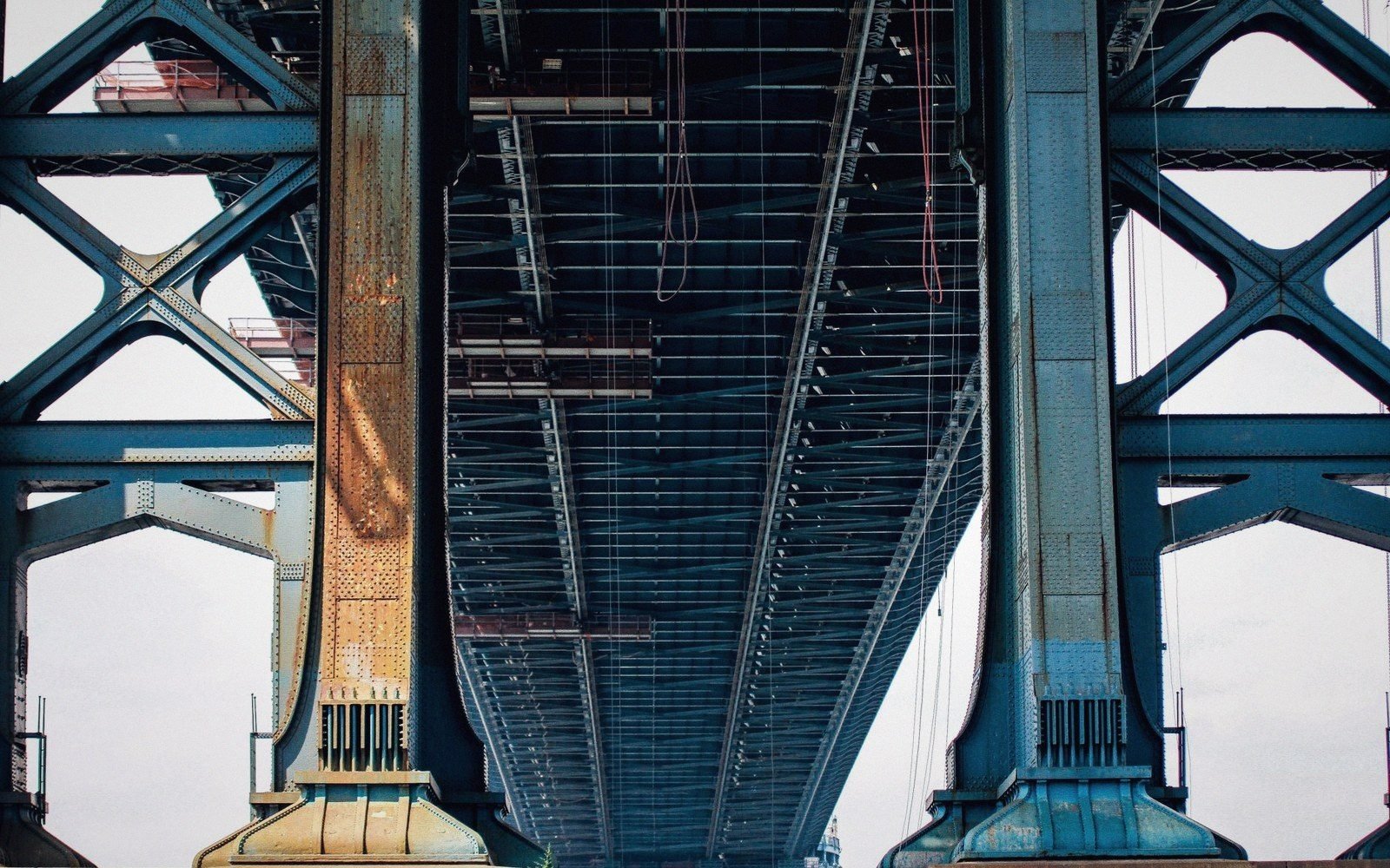Underside view of a steel truss bridge showing crisscrossed support beams and girders