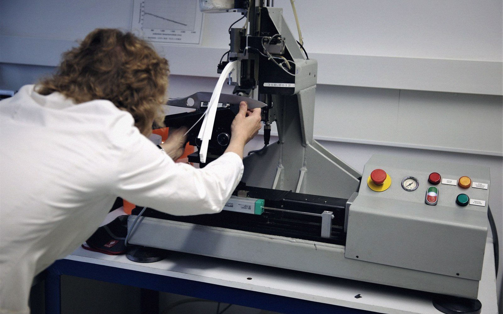 A lab technician tests a strip of material on a benchtop testing machine