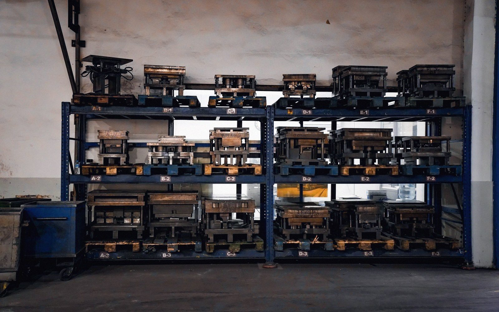 Metal molds and dies stored on labeled blue steel shelving in a workshop
