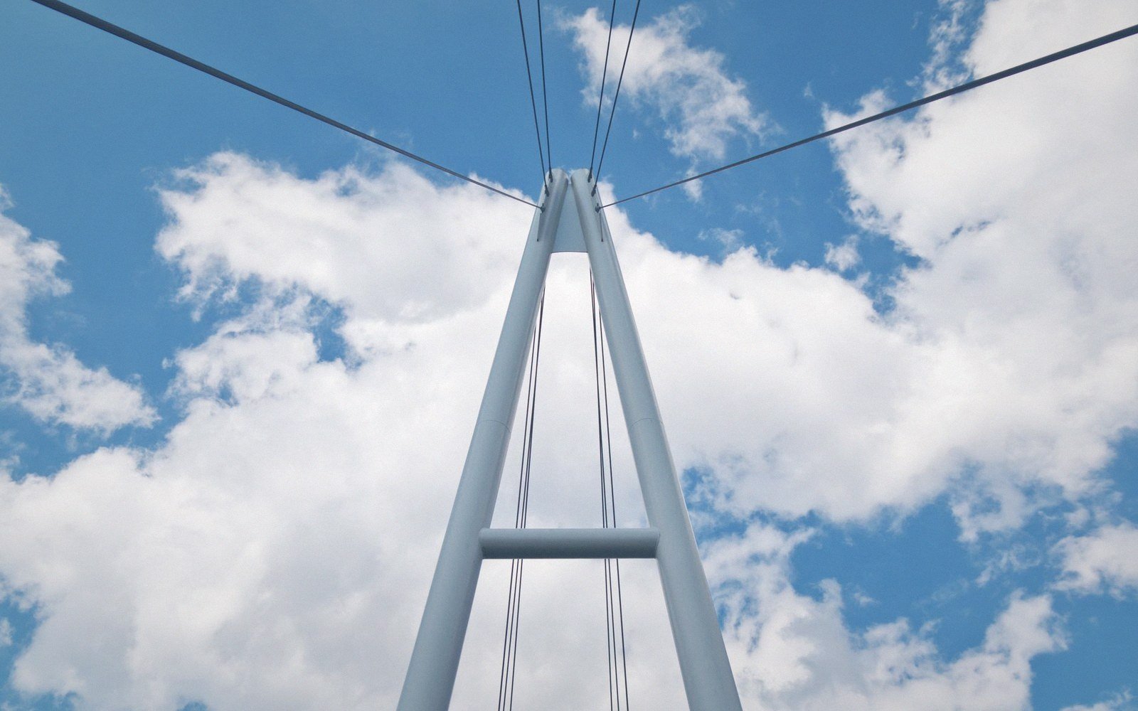 Upward view of a suspension bridge tower with cables against a cloudy sky