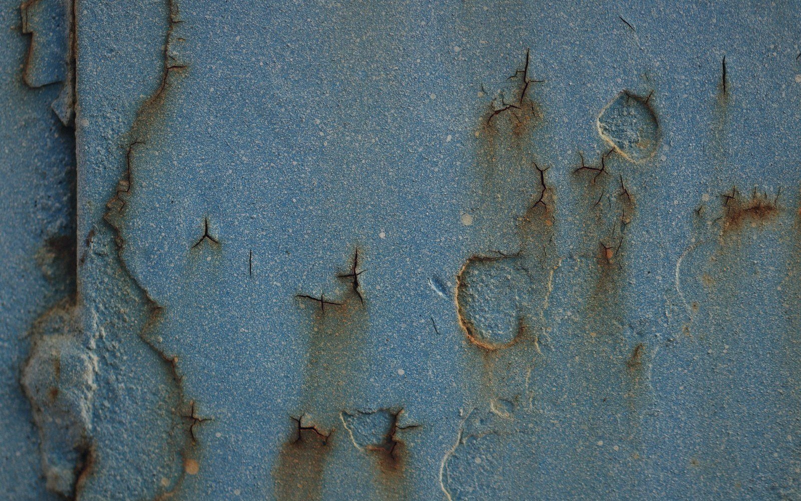 Blue paint peeling and cracking on rusted metal surface with dark corrosion spots