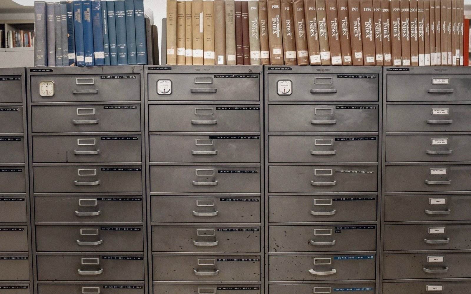 Rows of labeled metal filing cabinet drawers beneath shelves of bound index volumes